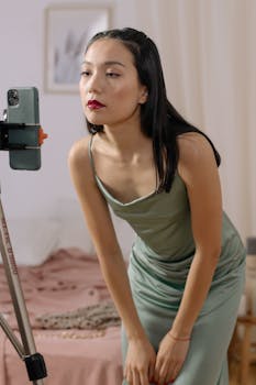 An Asian woman in a dress streaming live indoors using a cellphone.