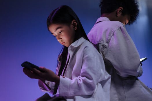 Two children engrossed in using their smartphones in a dimly lit setting.