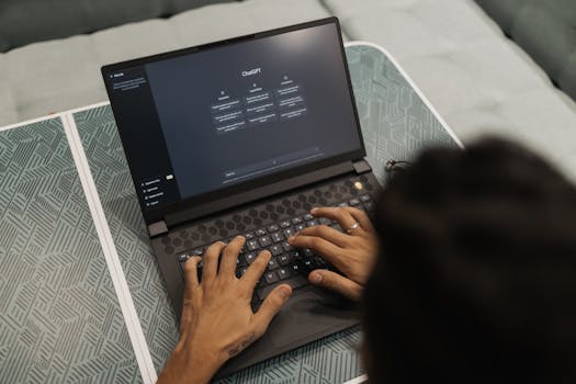 Close-up of hands typing on a laptop displaying ChatGPT interface indoors.