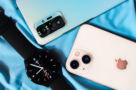 Close-up of smartphones and a smartwatch on blue fabric, showcasing technology essentials.