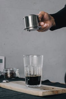 Hand hovering over a freshly brewed glass of coffee, capturing a morning ritual.